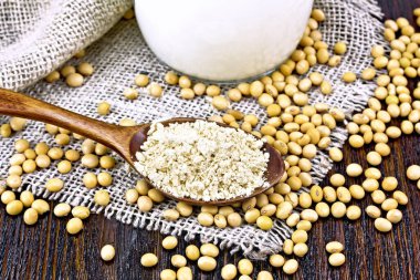 Soya unu kaşıkta, süt cam sürahide, soya fasulyesi çuval bezi ahşap tahtada.