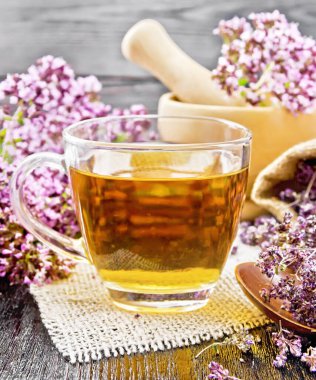 Çuval bezinde cam bir fincanda Oregano çayı, havanda taze çiçekler ve masada kurutulmuş kestane çiçekleri ve tahta arka planda kaşık.
