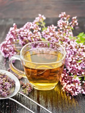 Cam bir fincanda Oregano bitkisel çayı, taze marjoram çiçekleri ve ahşap arka planda kurumuş çiçekli metal süzgeç.
