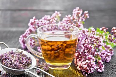 Cam bir fincanda Oregano bitki çayı, taze çiçekler ve koyu ahşap yaban domuzunda kurutulmuş mermer çiçekli metal süzgeç.
