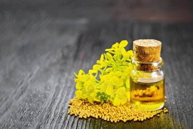 Cam bir şişede hardal yağı, tahıllar ve ahşap bir tahta üzerinde sarı çiçekler.