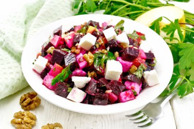 Pancar salatası, tuzlu peynir, elmalar, ceviz, maydanoz, balzamik sirke ve zeytinyağı ile tatlandırılmış bir tabak, bir havlu ve tahta bir arka planda çatal.