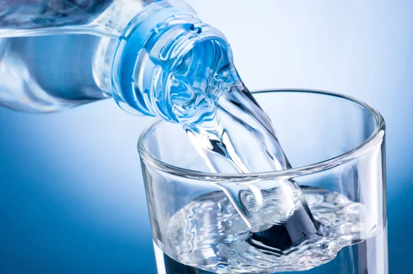 Nahaufnahme, wie man Wasser aus der Flasche in ein Glas auf blauem Hintergrund gießt — Stockfoto