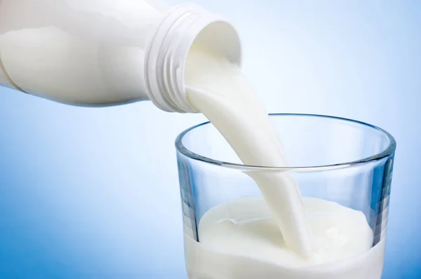 Hälla mjölk från vita plast flaska i glas på blå bakgrunds — Stockfoto