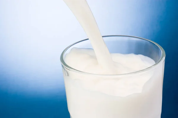 Milch in Glas auf blauem Hintergrund gießen — Stockfoto
