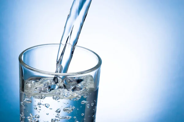 Gießen von Wasser in Glas auf blauem Hintergrund — Stockfoto