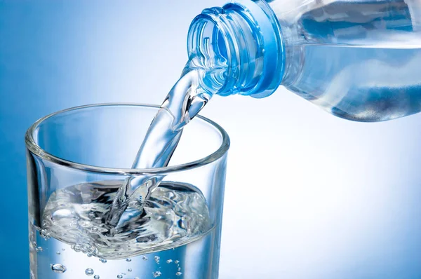 Wasser aus Flasche in Glas auf blauem Hintergrund gießen — Stockfoto
