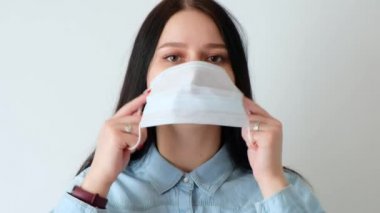 Uzun kahverengi saçlı, gülümseyen genç bir kızın yakın çekimi tıbbi koruyucu bir maske takıyor, kameraya bakıyor, covid-19 hijyen konsepti, koronavirüs, beyaz arka planda, beyaz duvar evi.