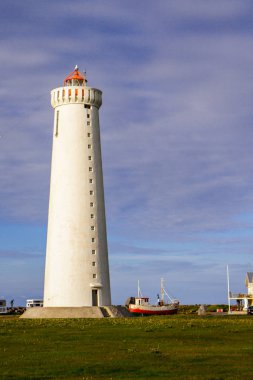 Bir deniz feneri ve bulutlu bir gökyüzü arka plan üzerinde bir tekne ile manzara. İzlanda