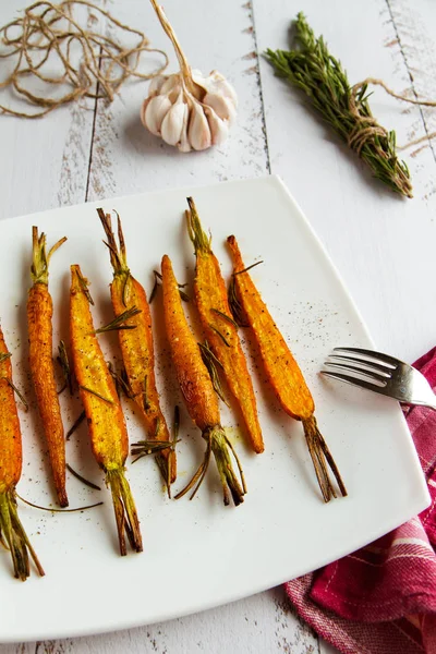 Carote arrosto con rosmarino e spezie su un piatto bianco Immagine Stock