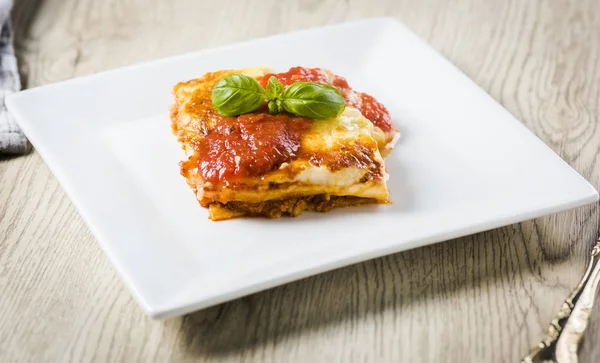 Porción apetitosa de lasaña en un plato blanco con salsa de tomate — Foto de Stock