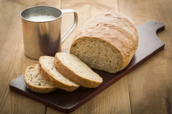 La hogaza del pan a la tabla y la leche — Foto de Stock