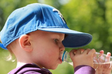 Çocuk parkta sıcak yaz aylarında bir plastik şişe suyu içer