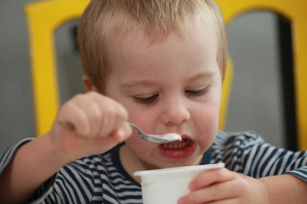 Engraçado bebê menino loiras lambe o dedo com iogurte — Fotografia de Stock
