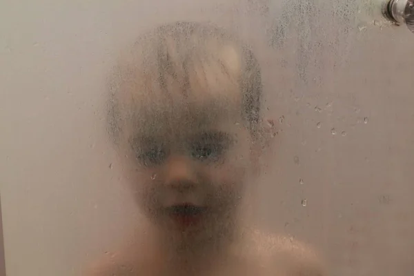 Baby pod prysznicem za szybą z kroplami — Zdjęcie stockowe