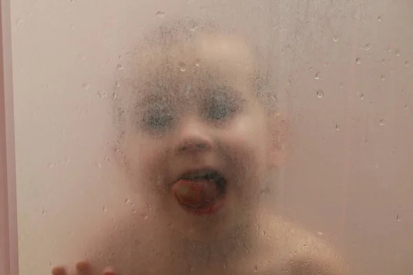 Bébé dans la douche derrière le verre avec des gouttes — Photo