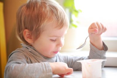 Çocuk masada oturan bir kaşık yoğurt yiyor