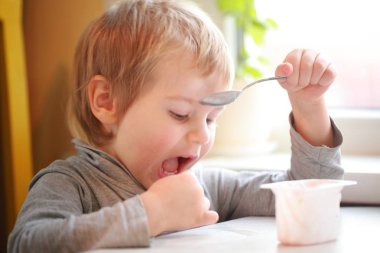 Çocuk masada oturan bir kaşık yoğurt yiyor