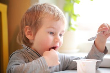 Çocuk masada oturan bir kaşık yoğurt yiyor
