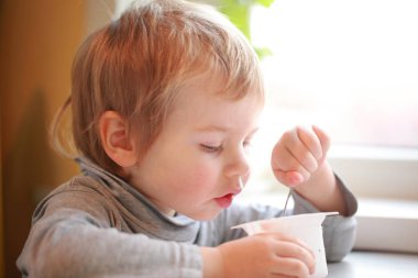Çocuk masada oturan bir kaşık yoğurt yiyor