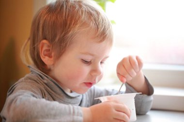 Çocuk masada oturan bir kaşık yoğurt yiyor
