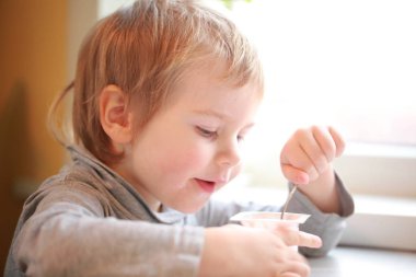 Çocuk masada oturan bir kaşık yoğurt yiyor