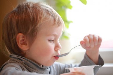 Çocuk masada oturan bir kaşık yoğurt yiyor