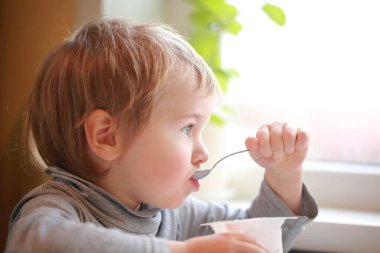 Çocuk masada oturan bir kaşık yoğurt yiyor