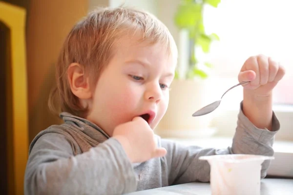 孩子吃酸奶时坐在桌旁 — 图库照片
