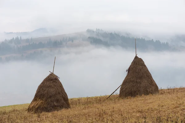 Paisaje otoñal con pajar y niebla en las montañas — Foto de Stock