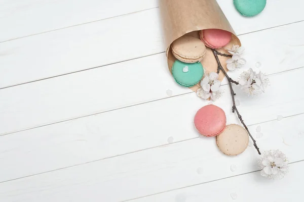 Package with colored macaroons and flowers on a white wooden bac — Stock Photo, Image