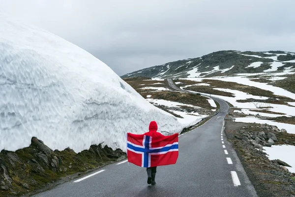 Menina com uma bandeira norueguesa em uma estrada nevada na Noruega — Fotografia de Stock