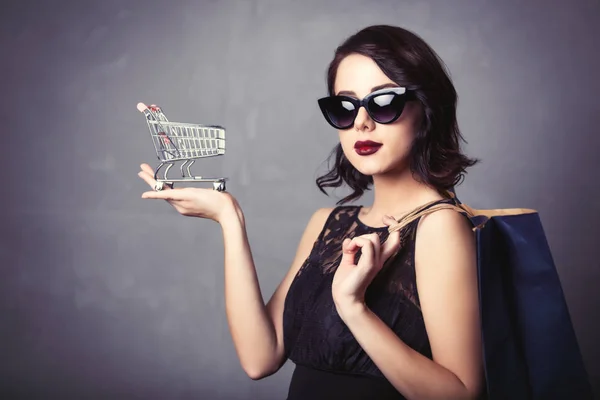 Mujer en vestido negro con carrito de la compra y bolsa —  Fotos de Stock