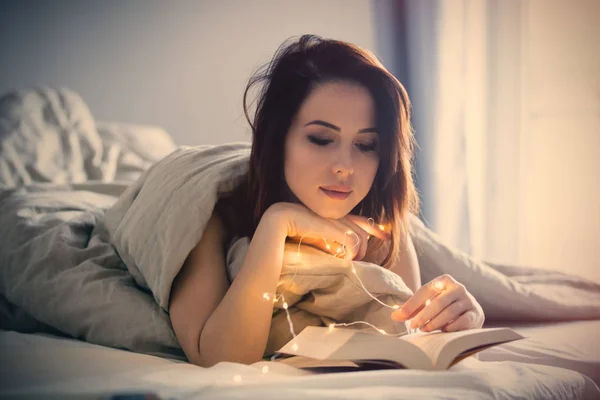 Vrouw met fairy lichten in bed — Stockfoto
