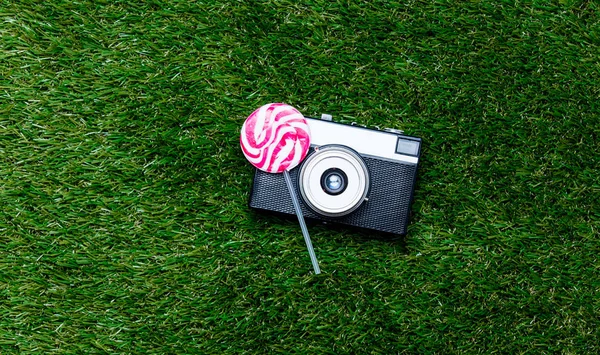 Vintage camera and lollipop candy on green grass background — Stock Photo, Image