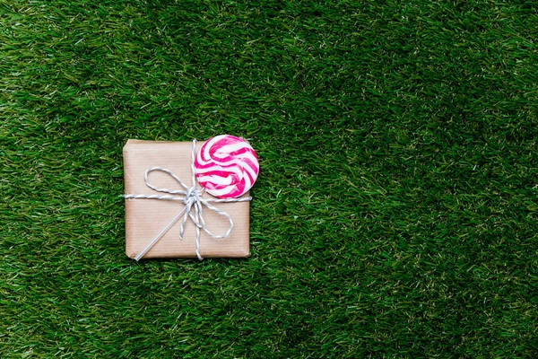 Hediye kutusu ve lolipop şeker POI yukarıda yeşil çim zemin üzerine — Stok fotoğraf