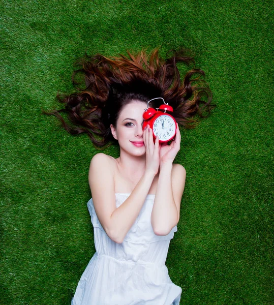 Retrato de una joven pelirroja con reloj despertador vintage acostada — Foto de Stock