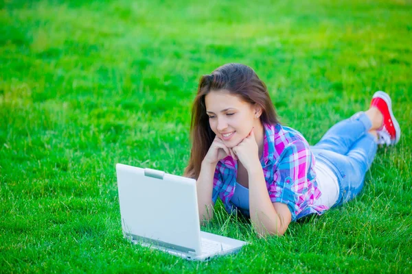 Flicka liggande på fältet med laptop — Stockfoto