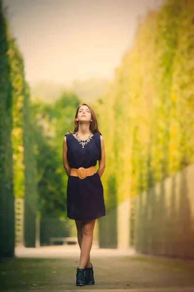 Beautiful young woman standing in the park full of bushes — Stock Photo, Image