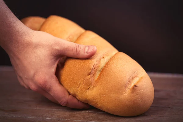 Мужская рука держит хлебный рулет на чудесном коричневом деревянном рюкзаке — стоковое фото