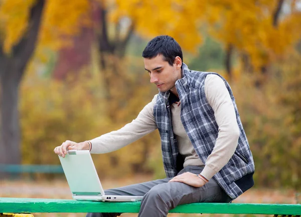 Фото красивого человека, сидящего на скамейке с ноутбуком на спине — стоковое фото