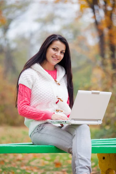 Φωτογραφία: όμορφη νεαρή γυναίκα που κάθεται στον πάγκο με φορητό υπολογιστή — Φωτογραφία Αρχείου