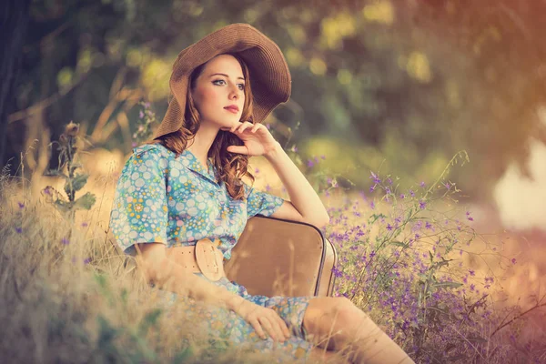 Foto de bela jovem com mala sentada no gras — Fotografia de Stock