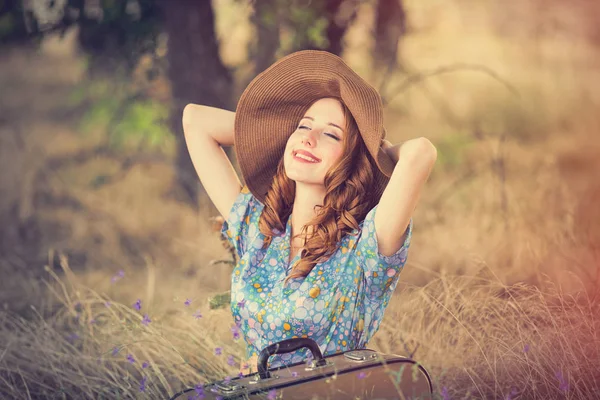 Foto van mooie jonge vrouw met koffer zittend op het gras — Stockfoto