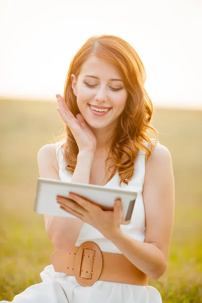Fotografie z krásné mladé ženy s tabletem, sedí v poli — Stock fotografie