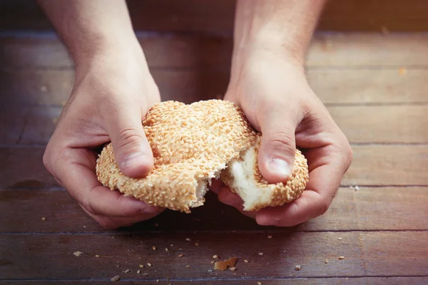 Manos rompiendo bollo fresco con sésamo — Foto de Stock