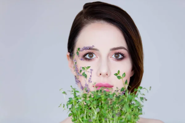 Krásná mladá žena s květinami na tvářích — Stock fotografie