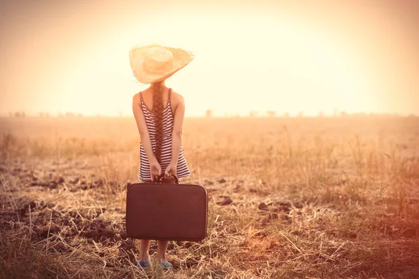 Девушка держит чемодан и стоит в поле — стоковое фото