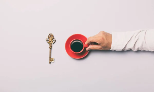 Hombre sosteniendo una taza de café rojo cerca de la llave dorada — Foto de Stock