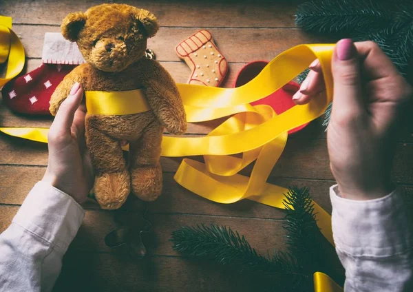 Hands wrapping christmas teddy bear and gifts — Stock Photo, Image